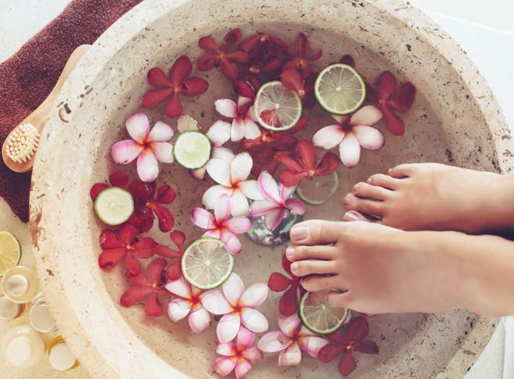 Frau nimmt ein Fußbad mit Blüten und Limetten und Zitronen