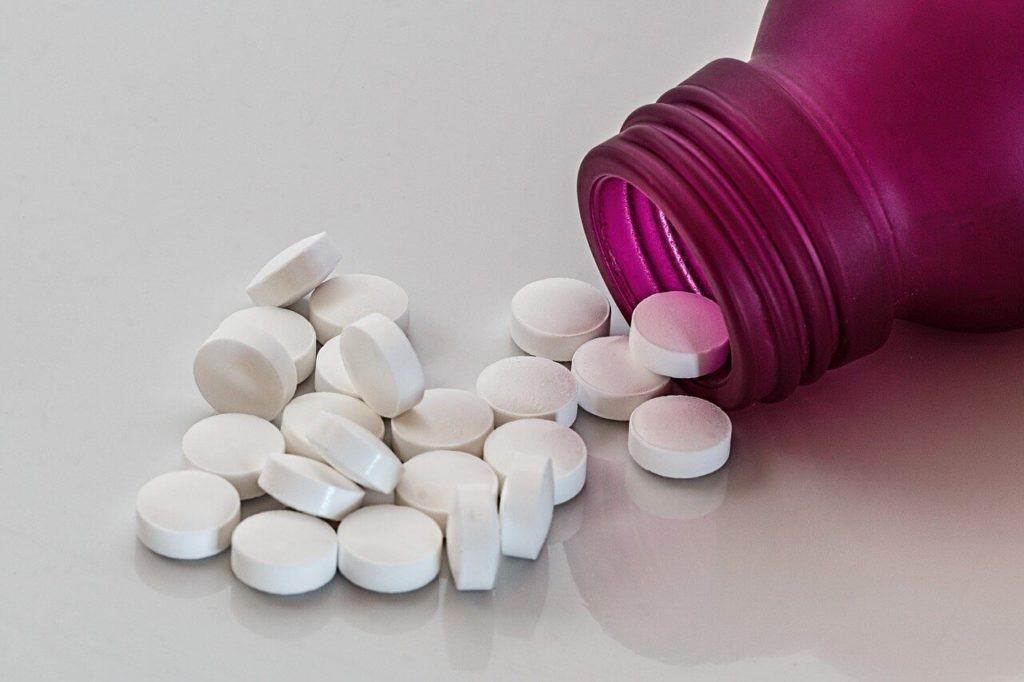 Viele weiße Tabletten neben einer geöffneten Tablettendose